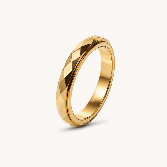 A gold band spinning ring from Anxiety Rings Australia with a geometric, faceted diamond-cut pattern on the exterior, shown standing upright on a clean off-white background.