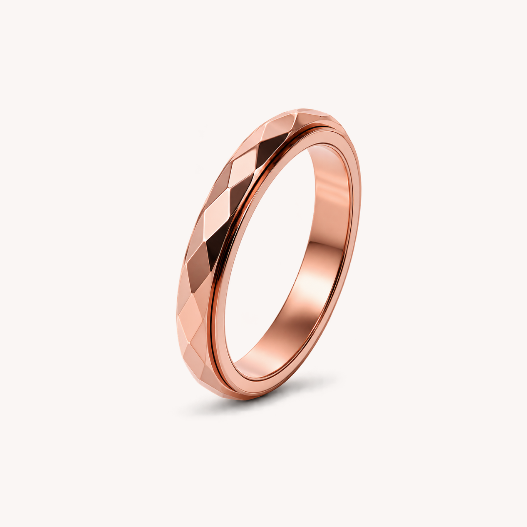 A rose gold band spinning ring from Anxiety Rings Australia with a faceted, diamond-cut geometric pattern, shown standing upright on a clean off-white background.