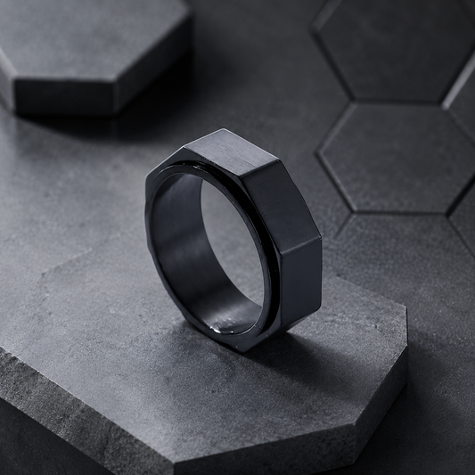 A dark metallic hexagonal spinning ring from Anxiety Rings Australia standing upright on a textured gray stone pedestal, with a matching dark gray hexagonal tile pattern in the background.