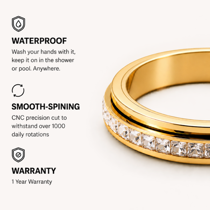 Gold spinner ring from Anxiety Rings Australia with a channel-set row of clear square-cut stones, shown on a light beige background with feature callouts reading WATERPROOF, SMOOTH-SPINING, and WARRANTY.