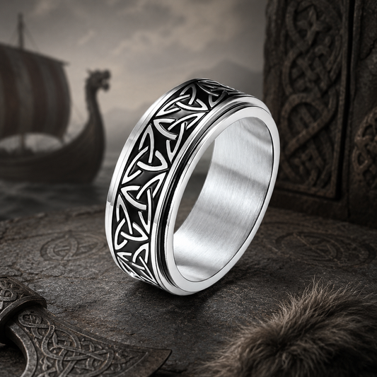 A silver-toned spinning ring from Anxiety Rings Australia with a black Celtic knot pattern on the outer band, shown on a viking background with a ship and fur coat as well as an axe
