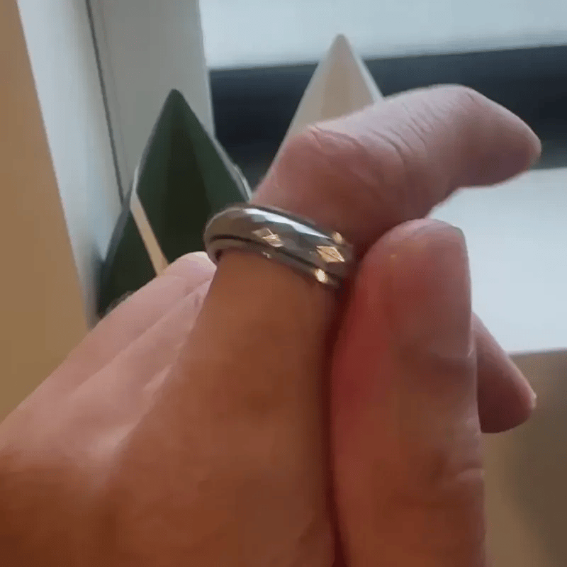 A close-up shot of a silver band spinning ring from Anxiety Rings Australia with a faceted, diamond-cut pattern worn on a person's finger.