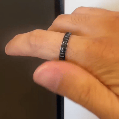 A close-up of a hand wearing a slim dark metallic spinning ring from Anxiety Rings Australia with a segmented, geometric design.