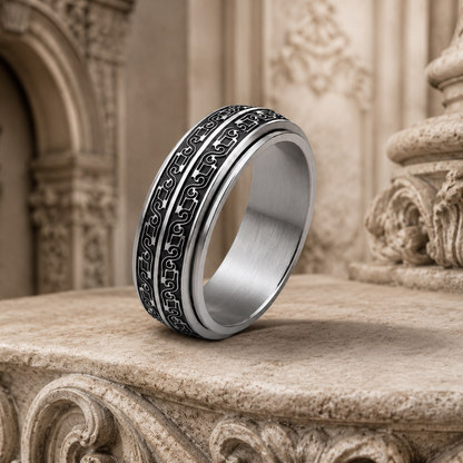 A silver-toned spinning ring from Anxiety Rings Australia with black engraved patterns, displayed on a beige stone architectural surface.